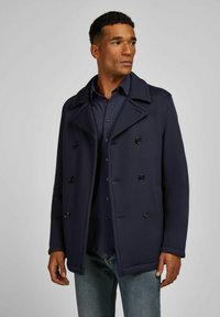 Marineblauer, doppelt geknöpfter Mantel mit großen schwarzen Knöpfen, spitzem Kragen und strukturiertem Stoff, getragen über einem dunklen Hemd und Jeans.