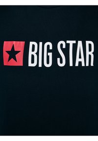 Crni materijal s bijelim tekstom "BIG STAR" i crvenim kvadratom koji s lijeve strane sadrži simbol crne zvijezde.