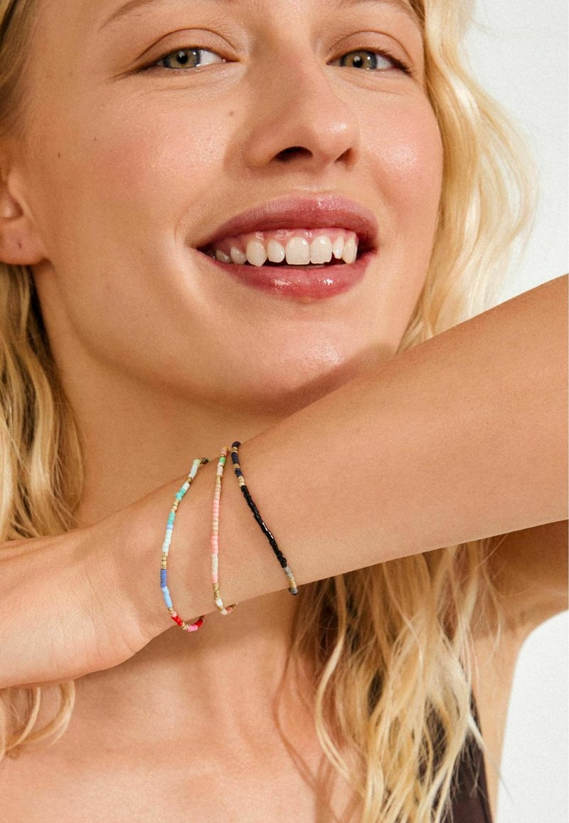 Värvilised helmestega käevõrud randmel; sisaldavad siniseid, roosasid, kollaseid, valgeid ja musti helmeid erinevates vormides ja suurustes. Sile pind.