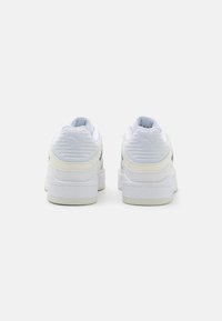 Hvite sneakers med en glatt skinnoverdel, polstret krage, strukturert hæl, grønne detaljer og en tykk gummisåle. Har logo på hælen.