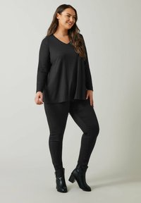 Mustapaita, jossa on pitkät hihat, V-pääntie ja ribbitekstuuri, yhdistettynä mustiin slim-fit-housuihin ja nilkkureihin. Yksinkertainen ja monochromaatinen muotoilu.