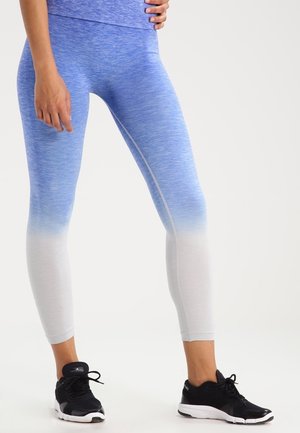 Leggings en degradado azul con tejido texturizado, que van de un azul más oscuro a blanco, combinados con zapatillas deportivas negras.