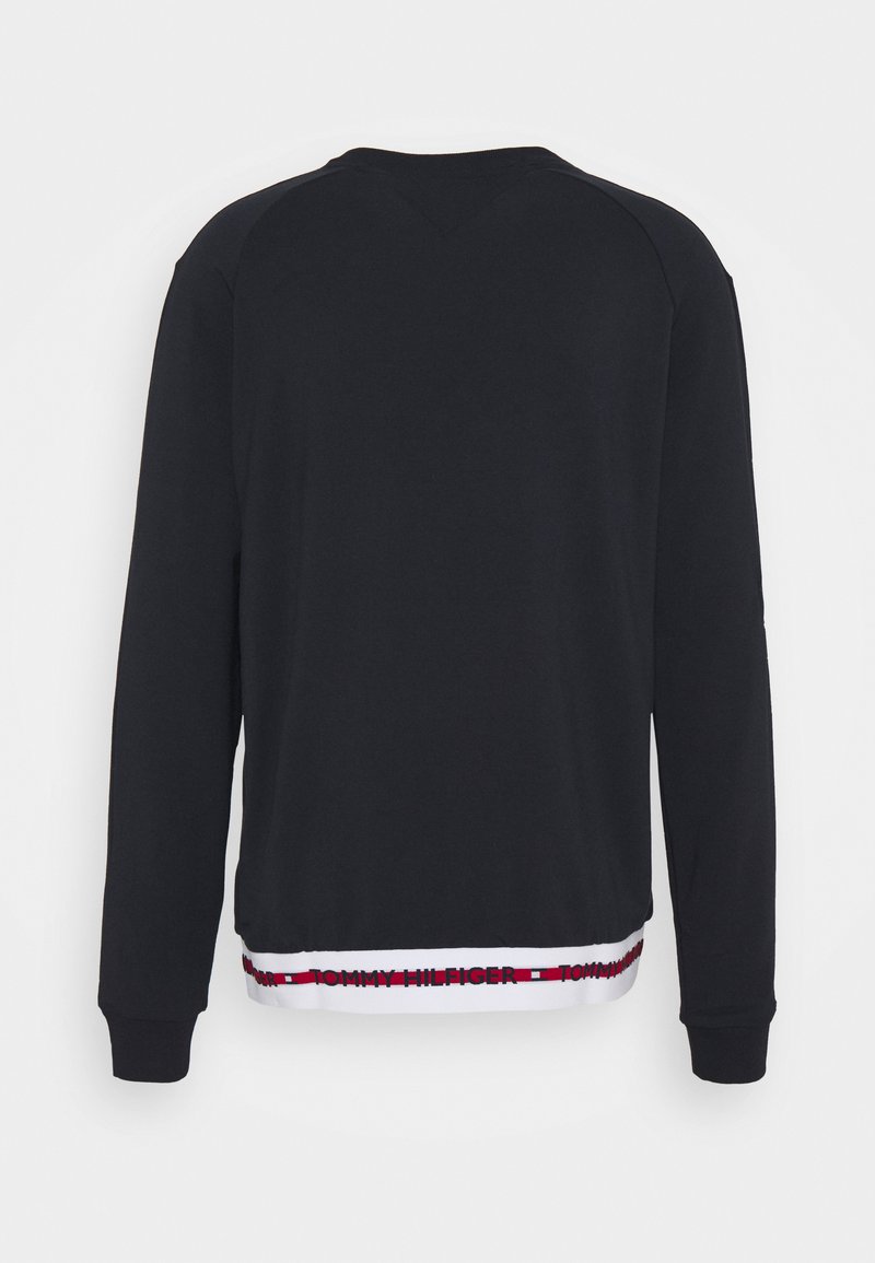Felpa nera a maniche lunghe con orlo bianco, caratterizzata da una fascia con il logo ripetuto di Tommy Hilfiger in rosso, bianco e blu nella parte inferiore.