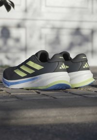Scarpe da ginnastica nere con accenti verdi, caratterizzate da una parte superiore testurizzata, suola imbottita e dettagli della suola blu e verde.