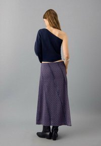 Navy cropped sweater with one shoulder exposed, paired with a purple patterned maxi skirt featuring circular designs, worn with black boots.