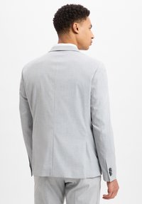 Grijze blazer in een lichtgewicht stof met een gestructureerde afwerking. Heeft een klassieke kraag, een getailleerde pasvorm en accenten met drie knopen bij de mouwen.