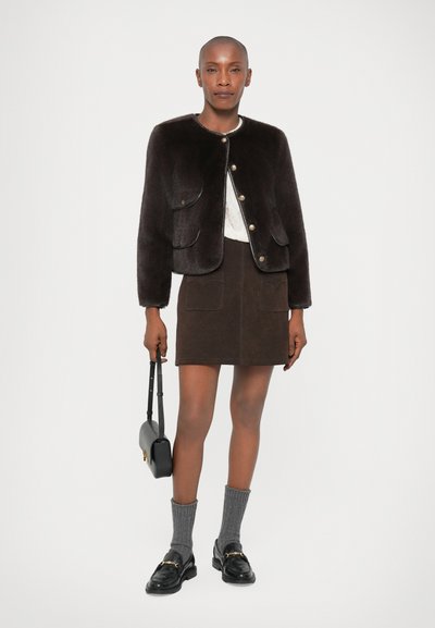 Brun kunstpelsjakke med gullknapper, kombinert med en brun suedeminiskjørt med to frontlommer og grå stripete sokker i svarte loafers.