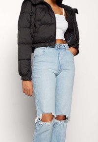 Černá zkrácená prošívaná bunda s zipovým zapínáním a bočními kapsami, v kombinaci s lehce modrými vysoce pasovými džíny s roztrhanými lemy.