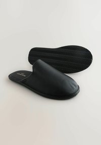Black leather slippers with a textured surface, rounded toe, and a flexible rubber sole featuring a herringbone pattern.