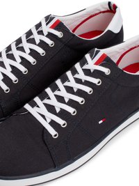 Ténis de lona azul escuro com atacadores brancos e solas de borracha. Inclui um design slip-on e um pequeno logótipo em vermelho, branco e azul.