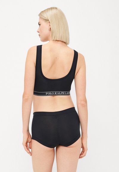 Sort atletisk bh med brede stropper, udstyret med et mærket elastisk bånd. Sammen med matchende sorte boyshorts, som begge er glatte og tætsiddende.