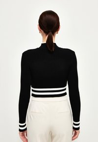 Schwarzer gerippter, kurzes Strickoberteil mit langen Ärmeln, verziert mit weißen horizontalen Streifen am Saum und an den Bündchen. Glatte Textur.