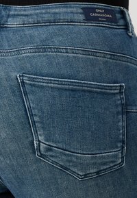 Blue denim jeans with a visible back pocket and a branded label at the waistband. The fabric shows a subtle texture and fading.