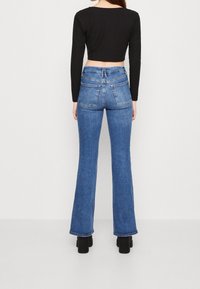 Åtsittande svart ribbad crop top och högmidjade blå jeans med utsvängd ben. Jeansen har två bakfickor och en slät yta. Svarta platåskor.