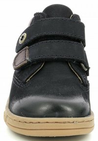 Zapato negro con dos correas de velcro, materiales de cuero y tela, punta redondeada y una suela de goma texturizada con un acento marrón claro.