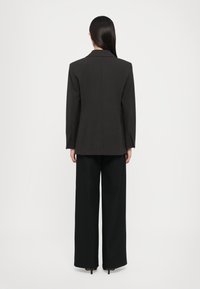 Blazer grigio con siluetta strutturata, con un'unica fessura sul retro, abbinato a pantaloni neri a gamba larga. Tessuto liscio e sartoriale.