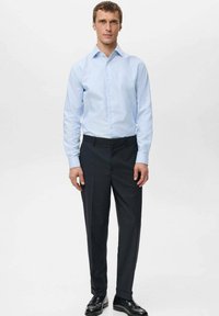 Svijetloplava prugasta košulja s ovratnikom na kopčanje u paru s tamnim hlačama. Glatki materijal i kroj po mjeri, upotpunjeni crnim cipelama.