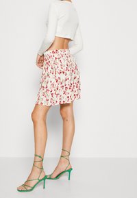 Blommig plisserad kjol i vitt med röda blommor, tillsammans med gröna strappy klackskor. Kortärmad topp som visar midjan.