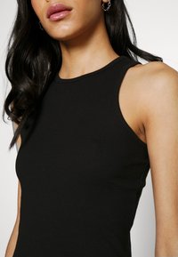 Débardeur noir côtelé avec une coupe ajustée, un col rond et des bretelles légèrement plus larges, présentant une texture lisse sans motifs apparents.