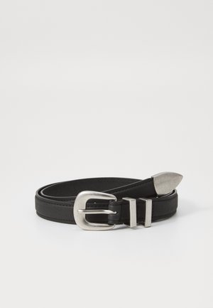Ceinture en cuir noir enroulée avec une boucle en métal argenté, deux passants et une pointe métallique sur fond uni.