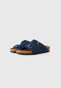 Marinblå mocka slide-sandaler med två justerbara spännen, korkfotbädd och svart gummisula på vit bakgrund.