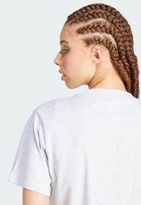 Camiseta de algodón gris con mangas cortas, cuello redondo y costuras visibles. El modelo tiene el cabello trenzado de forma elaborada.