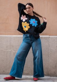 Knitted black sweater featuring large colorful floral embroidery in pink, yellow, and blue. Paired with wide-leg blue jeans and red flats.
