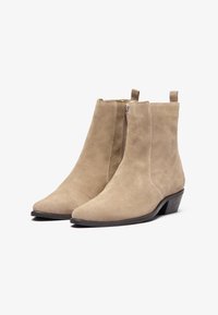 Botas de tobillo de ante beige con punta afilada, cremallera lateral y tacón bajo en bloque. Textura suave con un diseño minimalista.