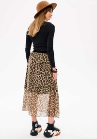 Leopardprint sheer maxi rok, zwart lange mouwen top, bruine hoed met brede rand, en zwarte chunky schoenen met crèmekleurige accenten.