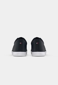Baskets noires avec une texture lisse, dotées d'une semelle en caoutchouc blanc et d'un design minimaliste. L'arrière présente un petit logo et des détails de couture discrets.