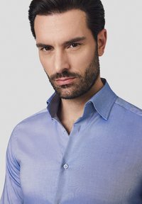 Jasnoniebieska koszula z bawełny, z klasycznym kołnierzykiem, zapięciem na guziki i subtelną fakturą. Brak widocznych wzorów lub akcentów.