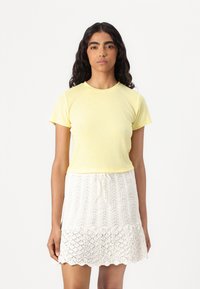 Camiseta de algodón amarilla de manga corta combinada con una falda blanca de punto con bordes en forma de onda y un patrón texturizado.