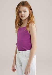 Lila ribbad linne kombinerat med vita högmidjade jeans. Linne har tunna band och en figurnära design, vilket skapar en enkel, modern look.