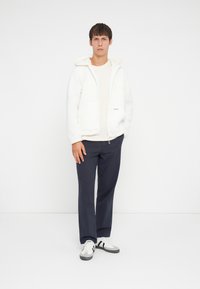 White fleece zip-up jacket with a hood, cream sweater, navy pants, and white sneakers with black stripes. Simple, casual outfit.