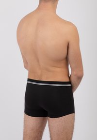 Boxer brev neri con una cintura morbida caratterizzata da una sottile striscia grigia, esposti su una schiena nuda, che mettono in risalto la texture liscia del tessuto.