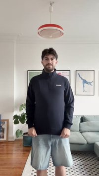 Melnas džemperis ar augstu apkakli, ar logotipu uz krūšu daļas, garām piedurknēm un brīvu piegriezumu. Pāris ar gaišiem denima šortiem un minimālistisku fonu.