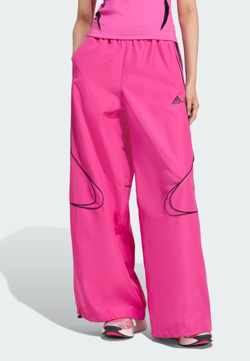 Bright pink, wide-leg pants made from lightweight material. Features black piping along the seams and side pockets. Adidas logo visible.