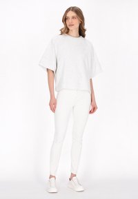 Lichtgrijs oversized t-shirt met korte mouwen, gecombineerd met witte slim-fit broek en witte sneakers. De stof lijkt zacht en casual te zijn.