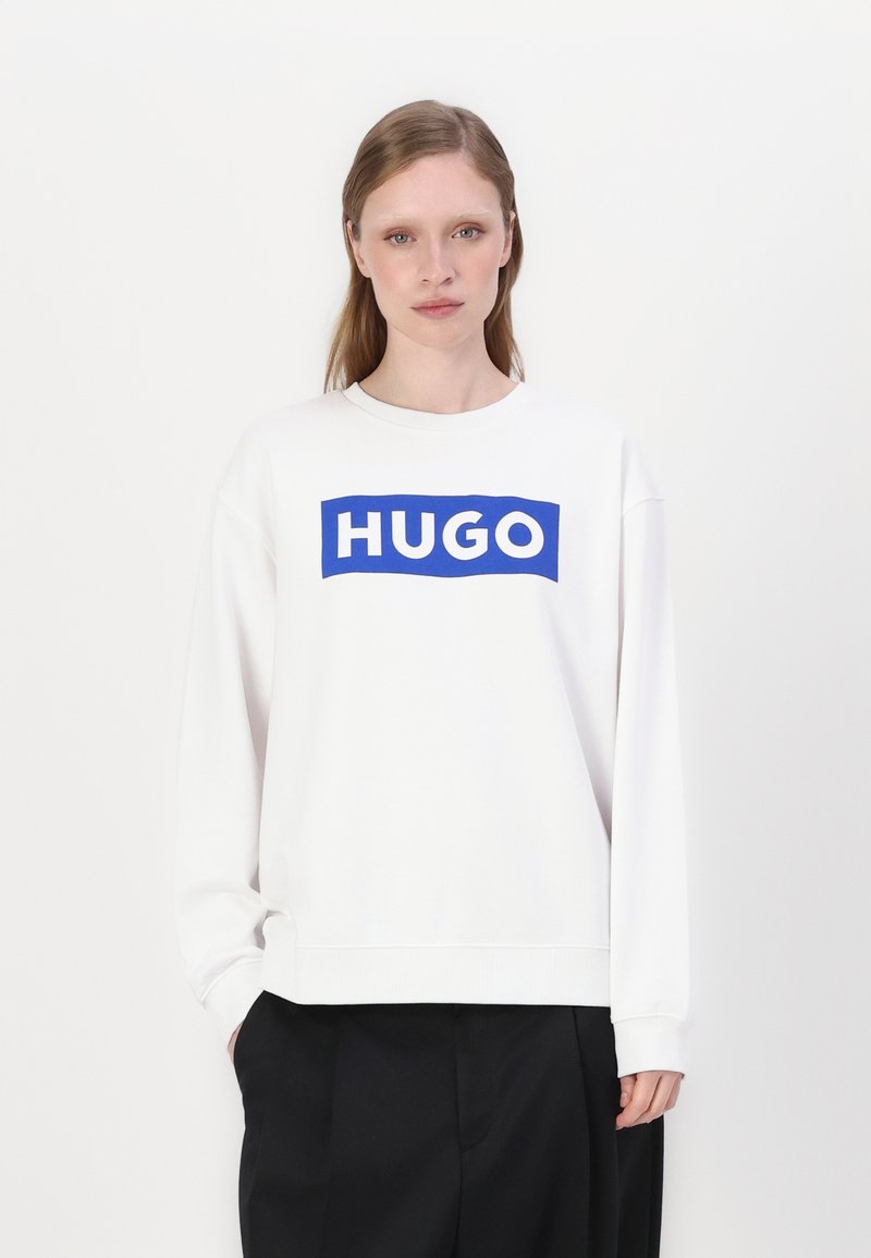 Biely sweatshir s modrým obdĺžnikovým grafickým prvkom s textom "HUGO." Klasický okrúhly výstrih, dlhé rukávy a uvoľnený strih.
