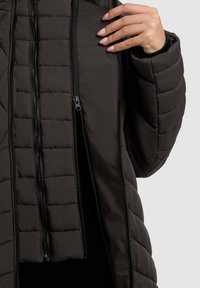 Hand adjusting the zipper of a dark quilted jacket with multiple parallel zippers, showing layered and padded texture.