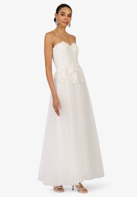 Robe blanche sans bretelles avec un corsage en dentelle florale et une jupe en tulle, présentant un décolleté en cœur et une broderie délicate, superposée pour plus de volume.