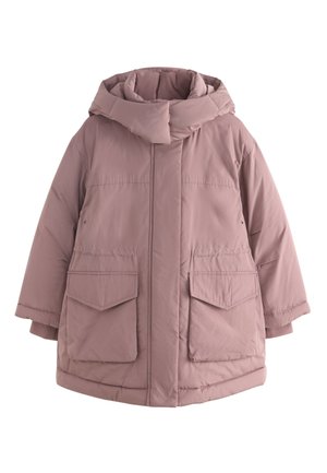 Kind mit lockigem Haar trägt eine mauvefarbene Kapuzen-Steppjacke, dunkelbraunen Cardigan, rosa Hemd und lockere hellblaue Jeans und steht mit den Händen in den Taschen.