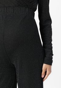 Melnas bodysuit ar garām piedurknēm, ar teksturētu virsmu, kas rotāta ar smalkiem sudraba punktiem un elastīgu jostasvietu.