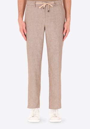 Pantaloni beige in lino con tasche frontali e coulisse beige in vita, indossati con sneaker bianche, mostrati dalla metà del busto ai piedi.