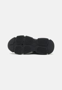 Svart sportsko såle med en teksturert mønster, som har dype spor for grep og en avrundet tådesign. Flat gummimateriale.