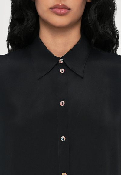 Camisa preta com botão, com colarinho pontiagudo, apresentando botões arredondados e multicoloridos e uma textura suave, semelhante a cetim.