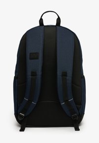 Granatowy plecak z czarną siateczkową tylną częścią, wyściełanymi paskami na ramiona i wyraźną metką. Posiada smukły design, co umożliwia wygodne noszenie.