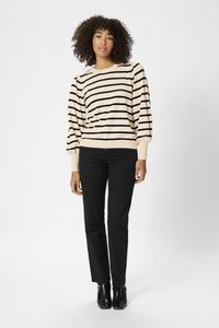 Maglione lavorato a maglia beige con strisce orizzontali nere, maniche lunghe a sbuffo e polsini a coste, abbinato a pantaloni neri a gamba dritta e stivali alla caviglia.