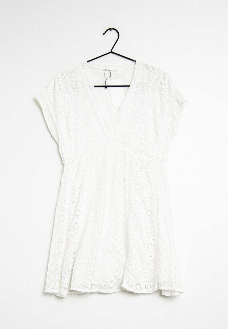 Robe blanche à manches courtes avec motifs en dentelle et col en V, suspendue sur un cintre noir sur un fond blanc uni.