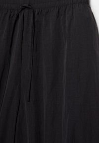 Jupe légère en tissu noir avec taille élastique et fine cordelette à nouer à l'avant.